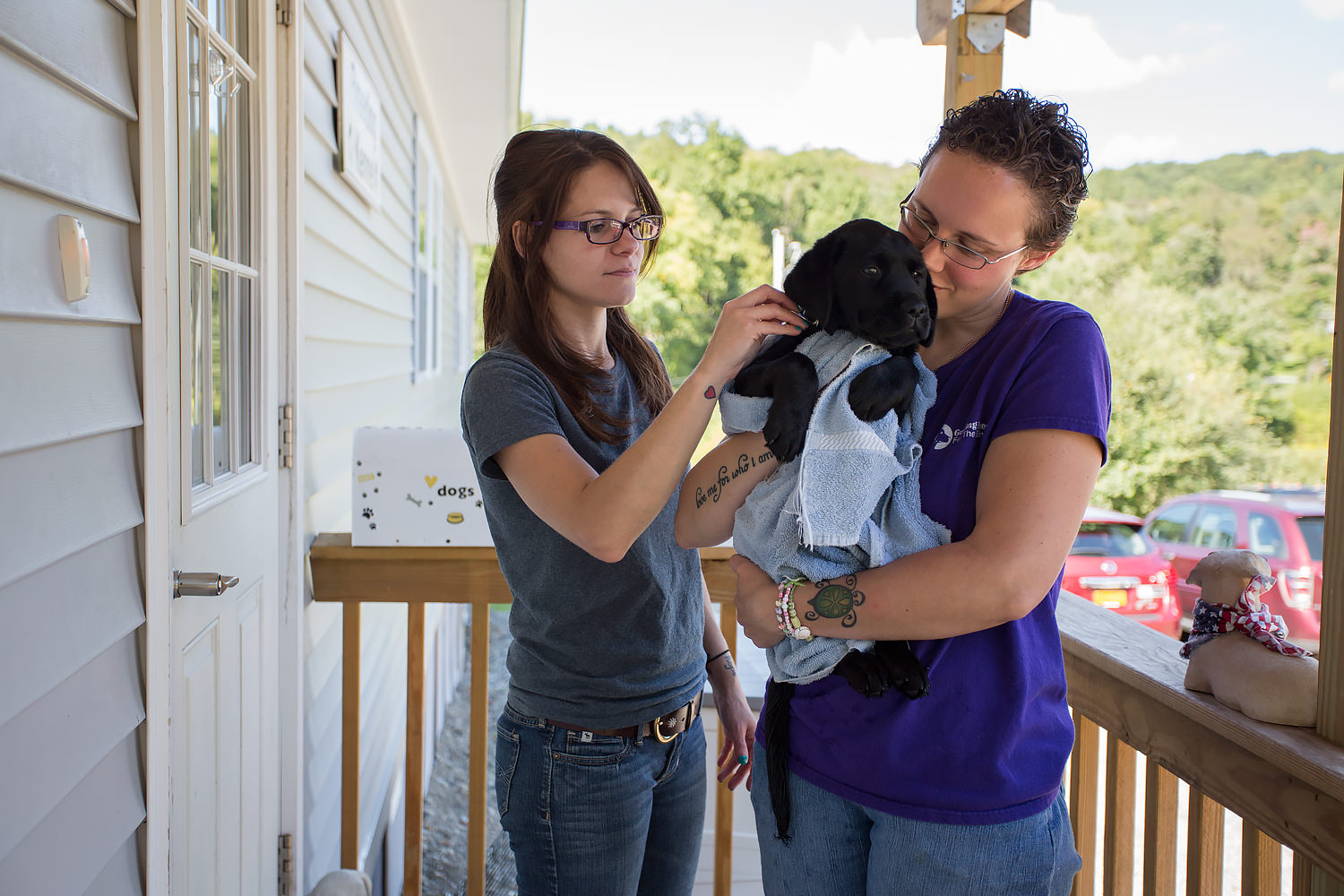 Guiding Eyes kennel techs standing on porch with black lab pup.